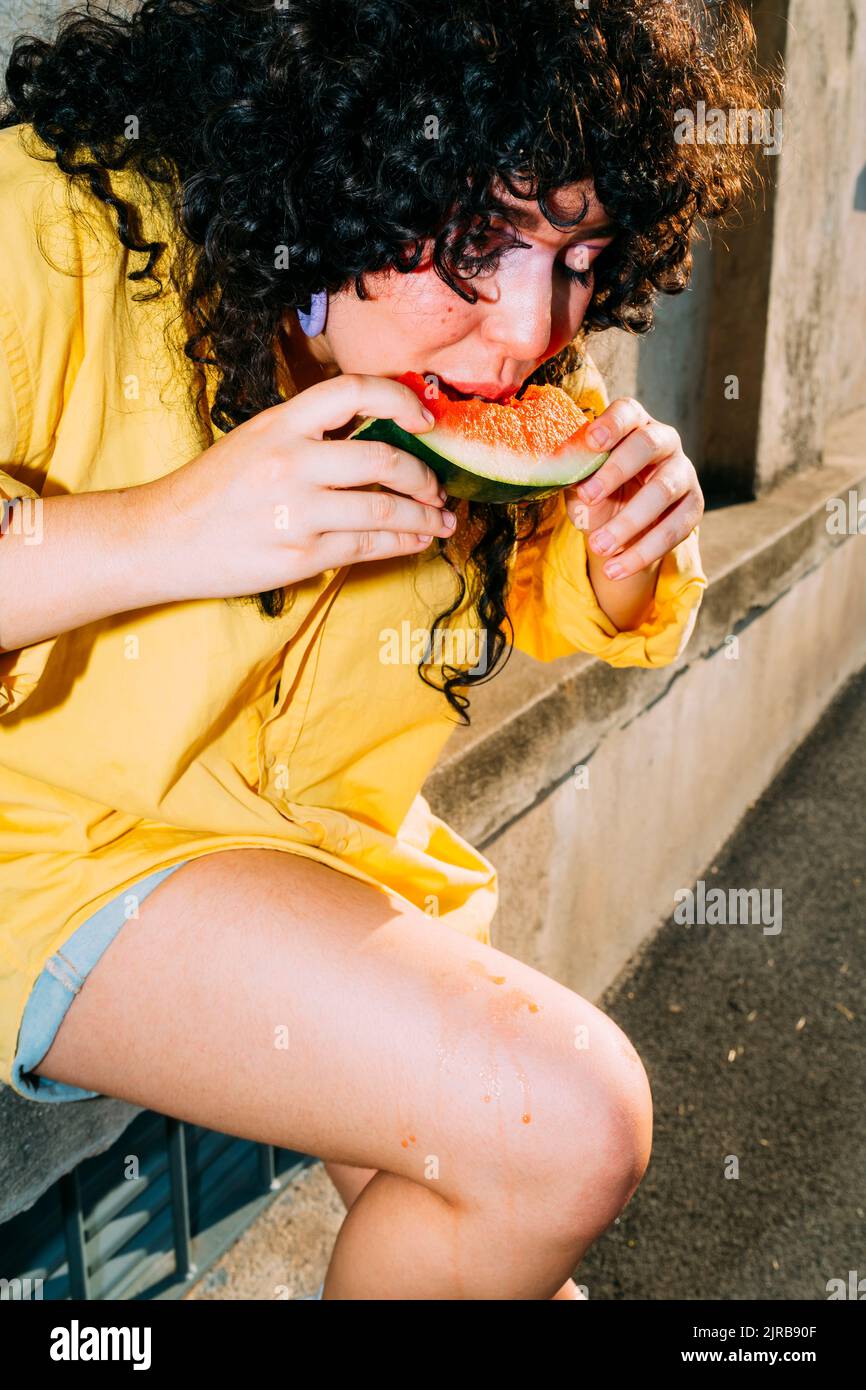 Donna che mangia la fetta di anguria seduta sulla panca Foto Stock