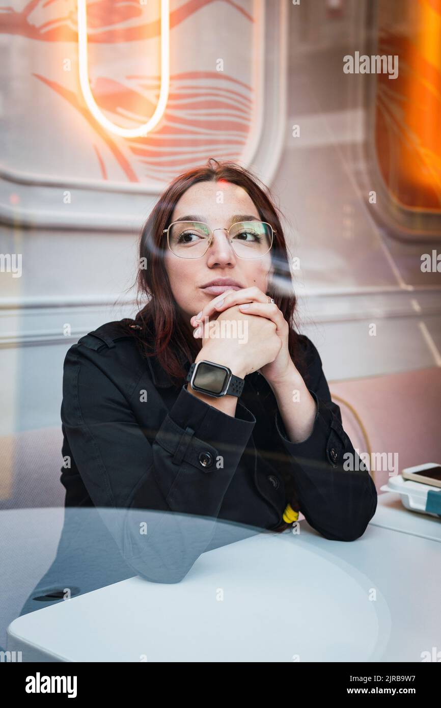 Giovane donna seduta in un caffè visto attraverso il vetro Foto Stock