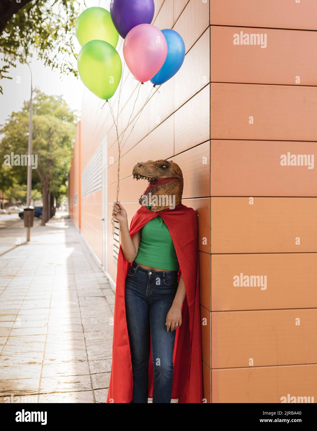 Giovane donna che indossa una maschera di coccodrillo in piedi con palloncini multicolore a parete Foto Stock