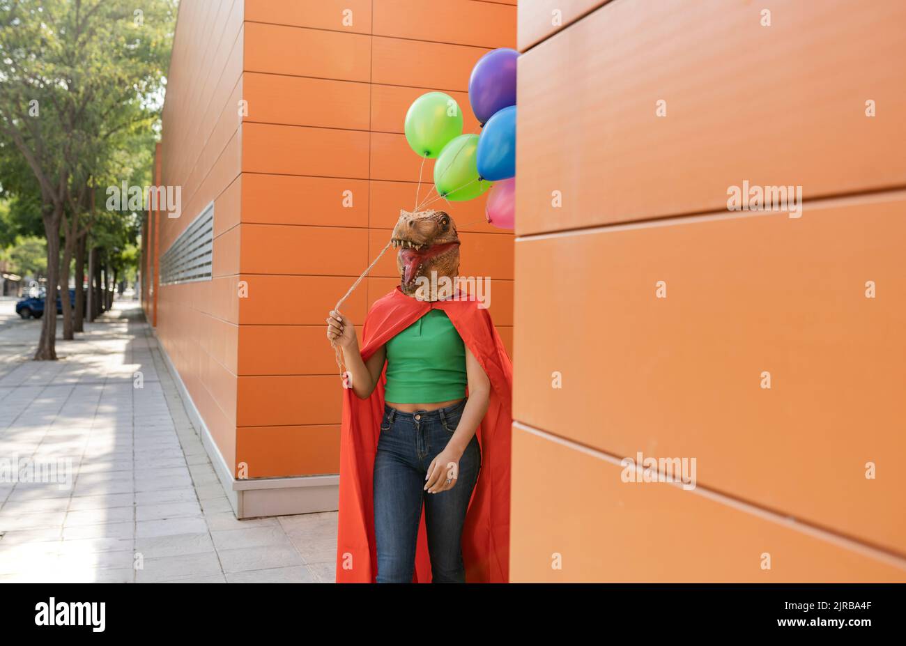 Donna che indossa una maschera di coccodrillo camminare con palloncini multicolore davanti al muro Foto Stock