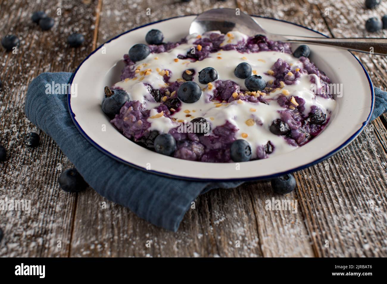 Porridge di mirtillo con noci tostate e yogurt isolato su un piatto di smalto vecchio stile su un tavolo di legno Foto Stock