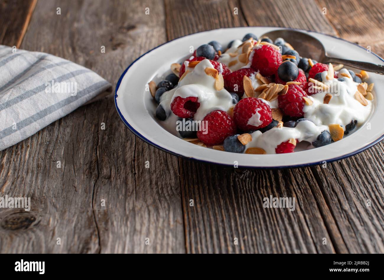 Yogurt con frutti di bosco e mandorle tostate per colazione a base di carb su tavolo in legno. Vista frontale Foto Stock