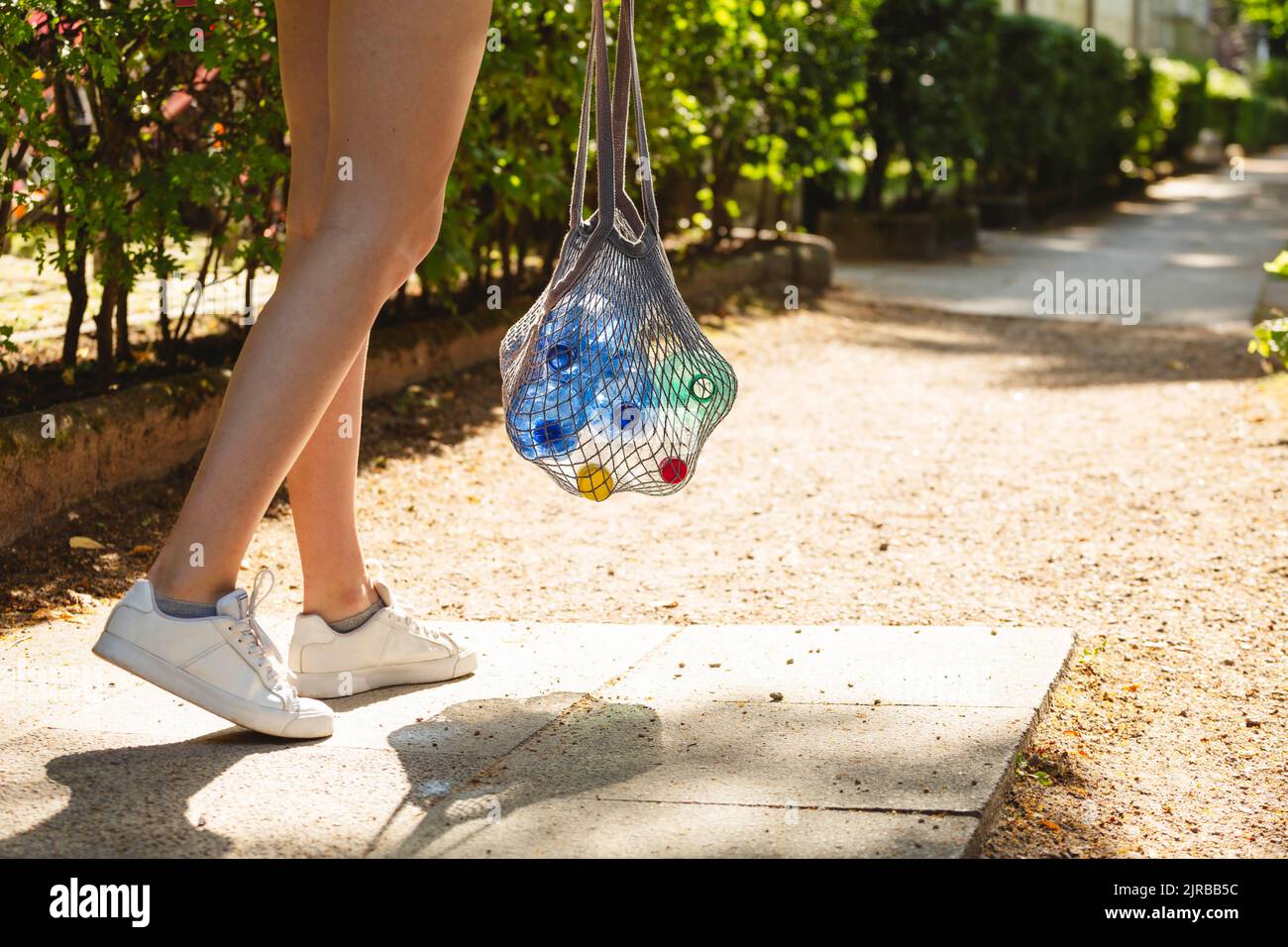 Ragazza che cammina sul sentiero che tiene il sacchetto di rete con bottiglie di plastica vuote Foto Stock