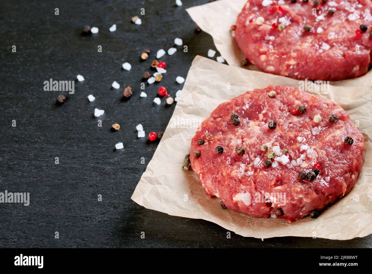 Hamburger di bistecca di manzo tritato fresco e crudo fatto in casa con spezie, su un tavolo nero ardesia, spazio copia Foto Stock