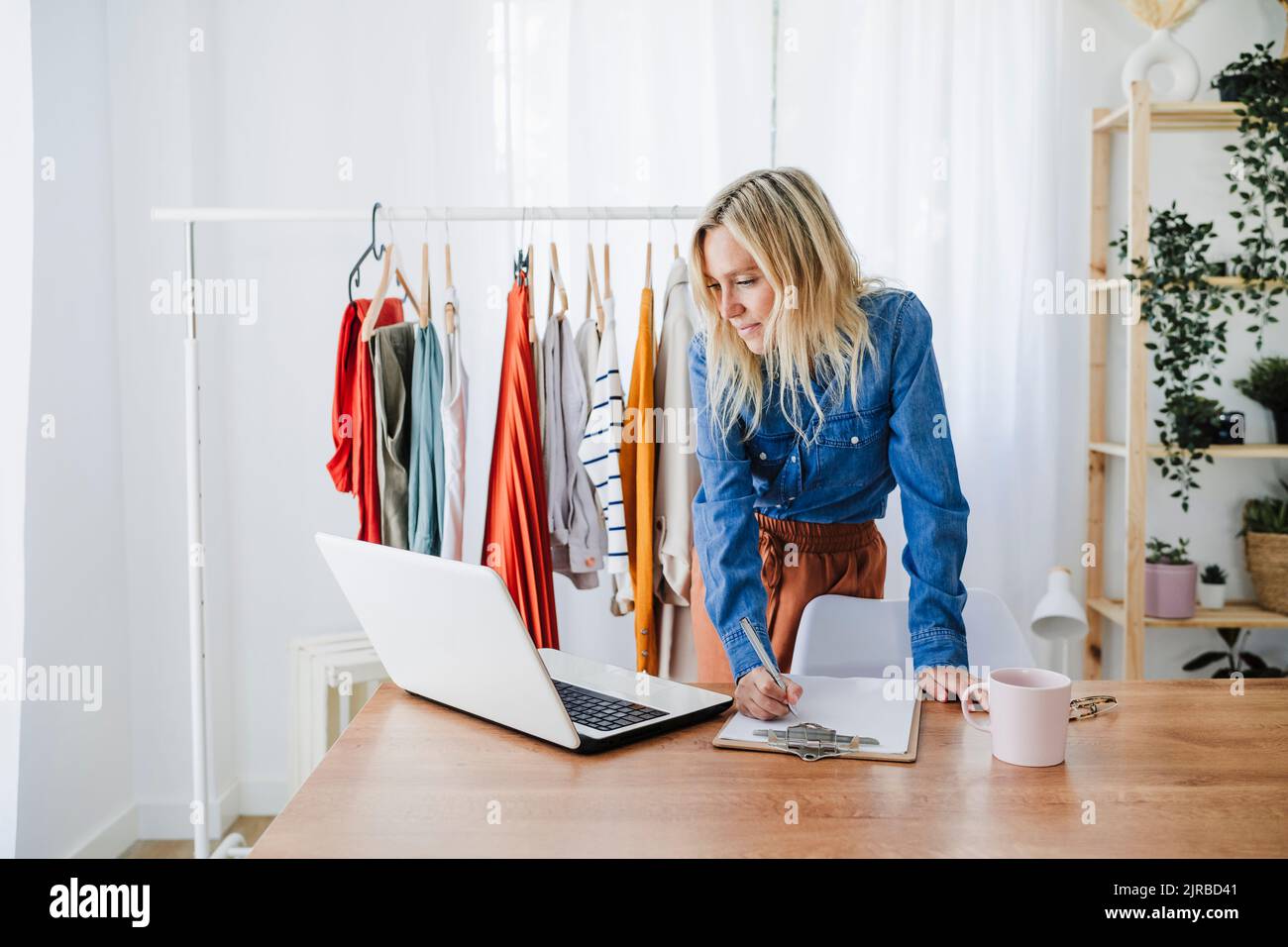 Stilista di moda scrivere su appunti guardando il portatile in casa ufficio Foto Stock