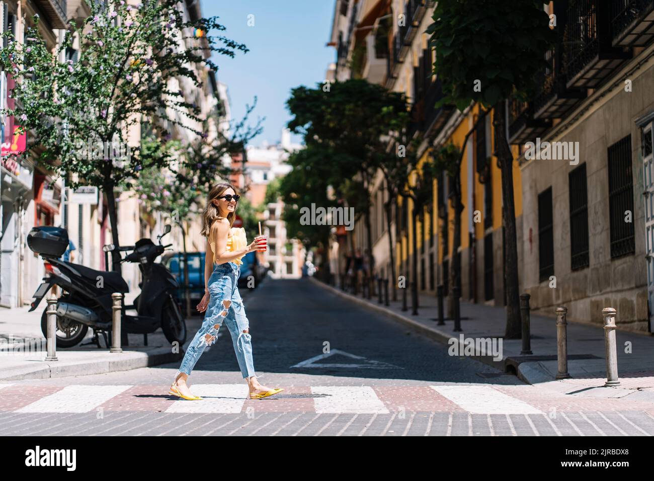 Donna che cammina con un drink in mano per strada il giorno di sole Foto Stock