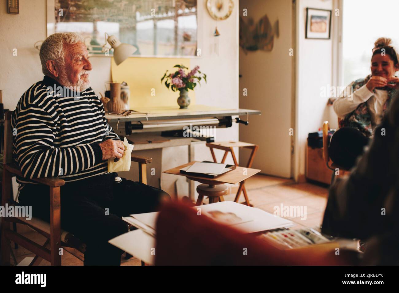 Uomo anziano sorridente seduto da artisti a casa Foto Stock