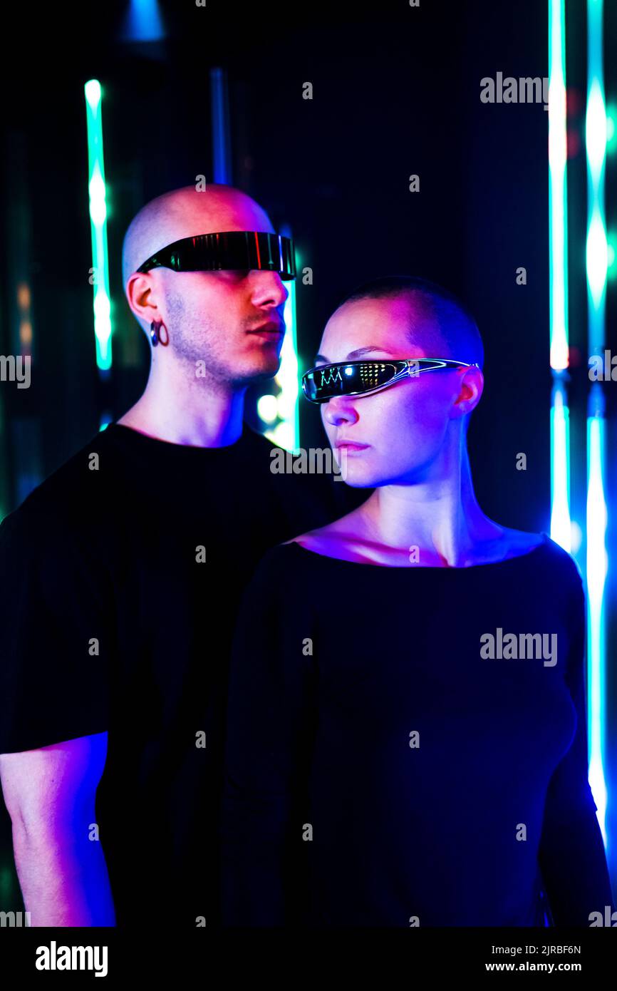 Uomo e donna che indossano occhiali intelligenti davanti all'illuminazione al neon Foto Stock