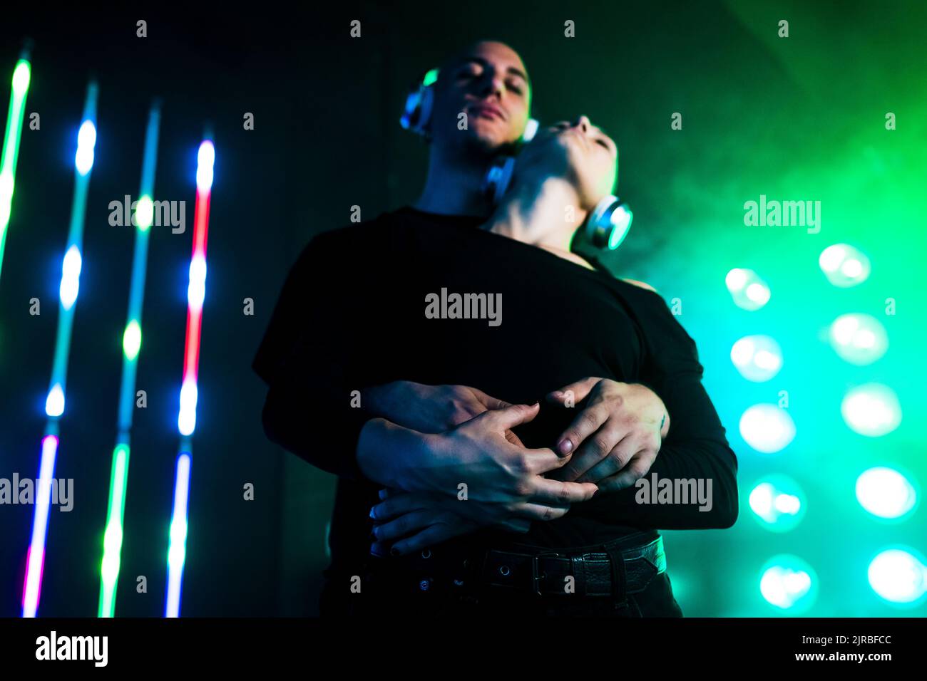 Coppia indossando le cuffie che si avvolgono davanti alle luci accese Foto Stock