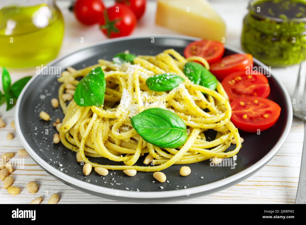 Pasta tradizionale italiana con verdure fresche, parmigiano, foglie di basilico, pinoli e salsa al pesto in piatto nero su fondo di legno bianco. Foto Stock