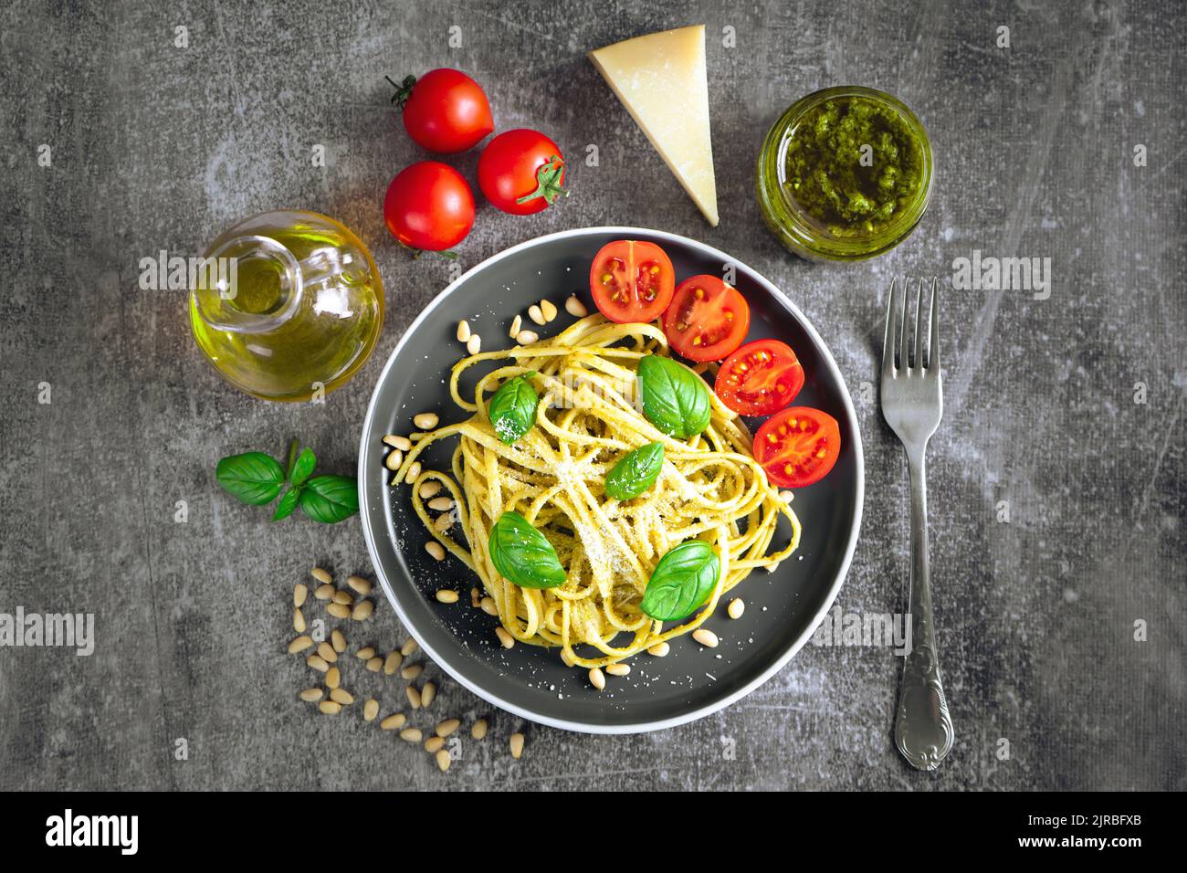 Pasta tradizionale italiana con verdure fresche, parmigiano, foglie di basilico, pinoli e salsa al pesto in ciotola nera su fondo di pietra grigia. In alto Foto Stock