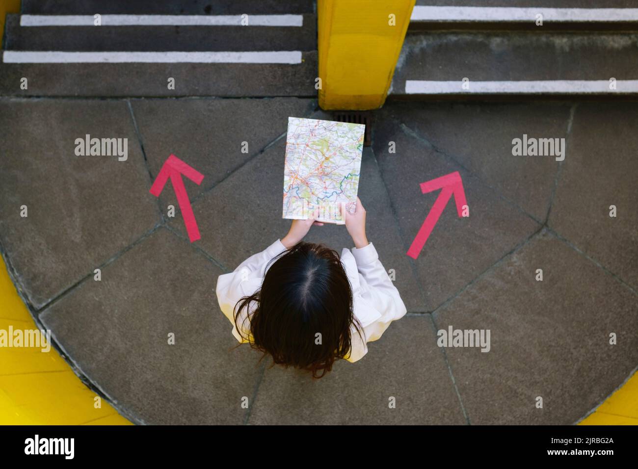 Giovane donna che legge la mappa in piedi tra i simboli delle frecce Foto Stock