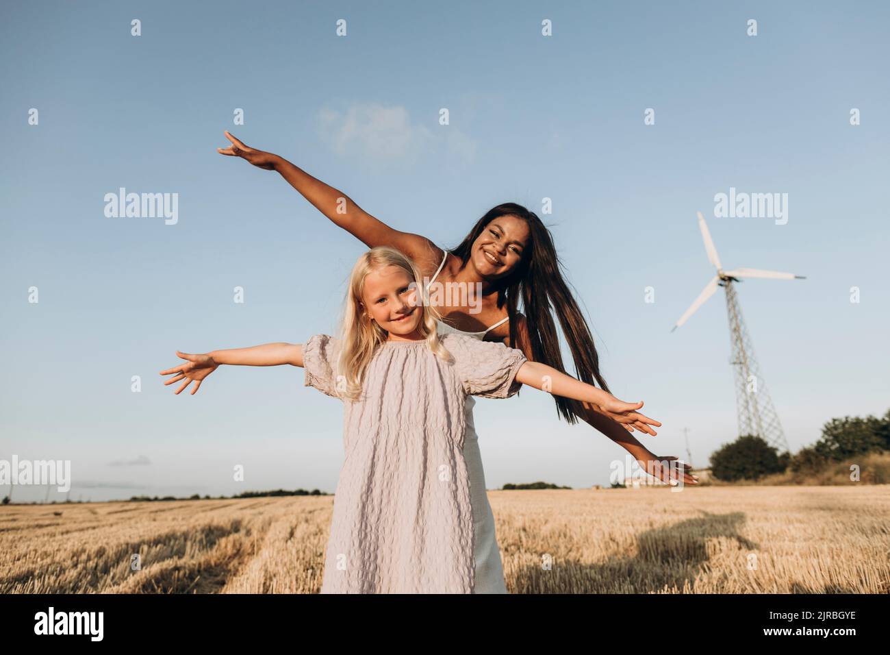Felice donna e ragazza con le braccia tese in piedi in fattoria di fronte al cielo Foto Stock
