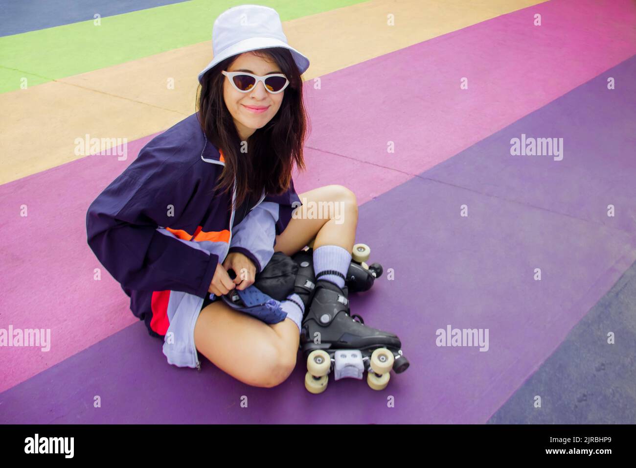 Donna sorridente che indossa pattini a rotelle seduti su un pavimento multicolore Foto Stock