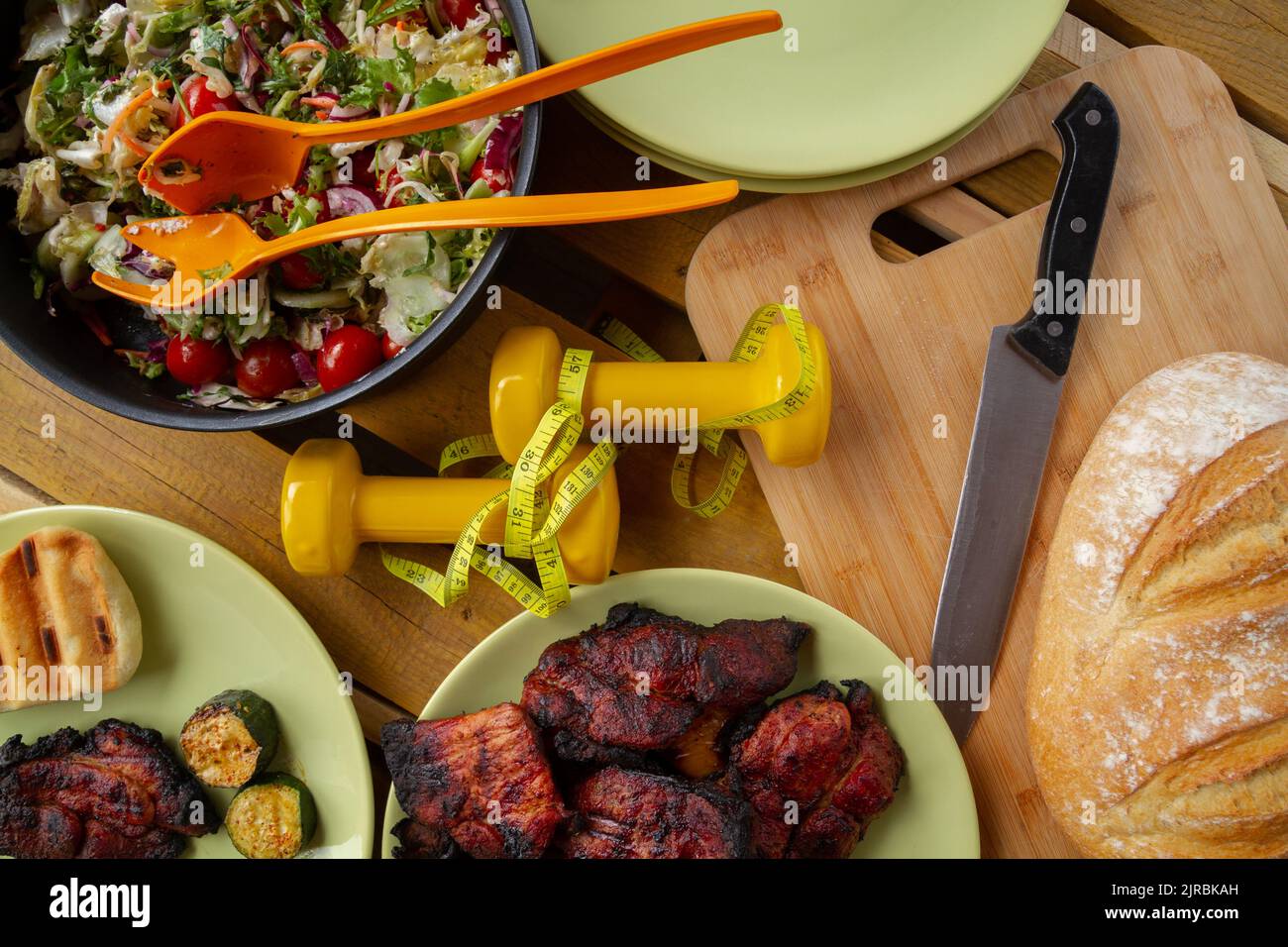 Manubri con metro a nastro, insalata di verdure, pane, carne di maiale alla griglia dal barbecue. Fitness gym griglieria concetto di festa, sana o cattiva scelta di dieta. Foto Stock