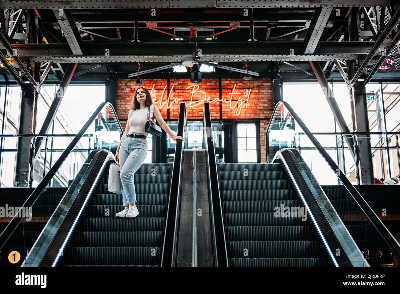 Giovane brunetta Latina attraente donna con borse per la spesa su scala mobile nel centro commerciale della moda. Foto Stock