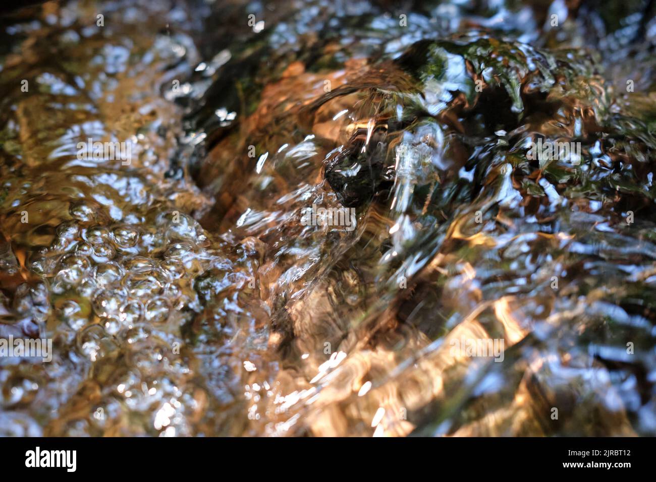 Le acque fluiscono e i riflessi del sole in un torrente in primo piano Foto Stock