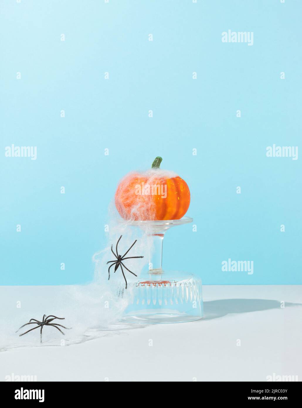 Concetto di Halloween minimale e spoky fatto di zucca su un podio di vetro con ragnatela e ragni su sfondo blu cielo. Idea creativa di vacanza. Centro di copiatura Foto Stock