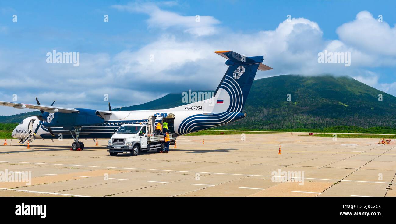 Mendeleevo, Russia - 29 luglio 2022: Scarico bagagli dall'aereo della compagnia aerea Aurora all'aeroporto di Kunashir isola, Mendeleev vulcano è di fronte Foto Stock