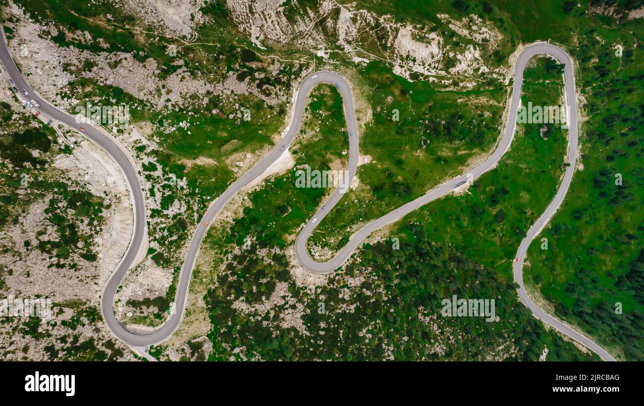 Strada tortuosa dall'alto valico delle Dolomiti. Grande viaggio su strada attraverso fitti boschi e prati. Vista aerea. Strada curvy in foresta estiva sc Foto Stock