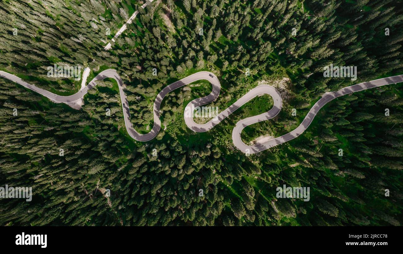 Strada tortuosa dall'alto valico delle Dolomiti. Grande viaggio su strada attraverso fitti boschi e prati. Vista aerea. Strada curvy in foresta estiva sc Foto Stock