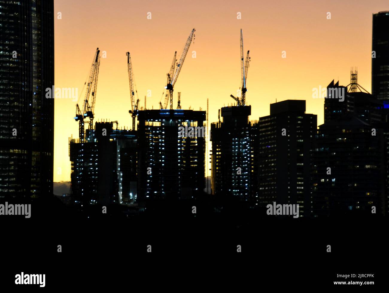 Skyline del CBD di Brisbane in silhouette con gru da costruzione al tramonto con luci accese nelle torri dei grattacieli Foto Stock