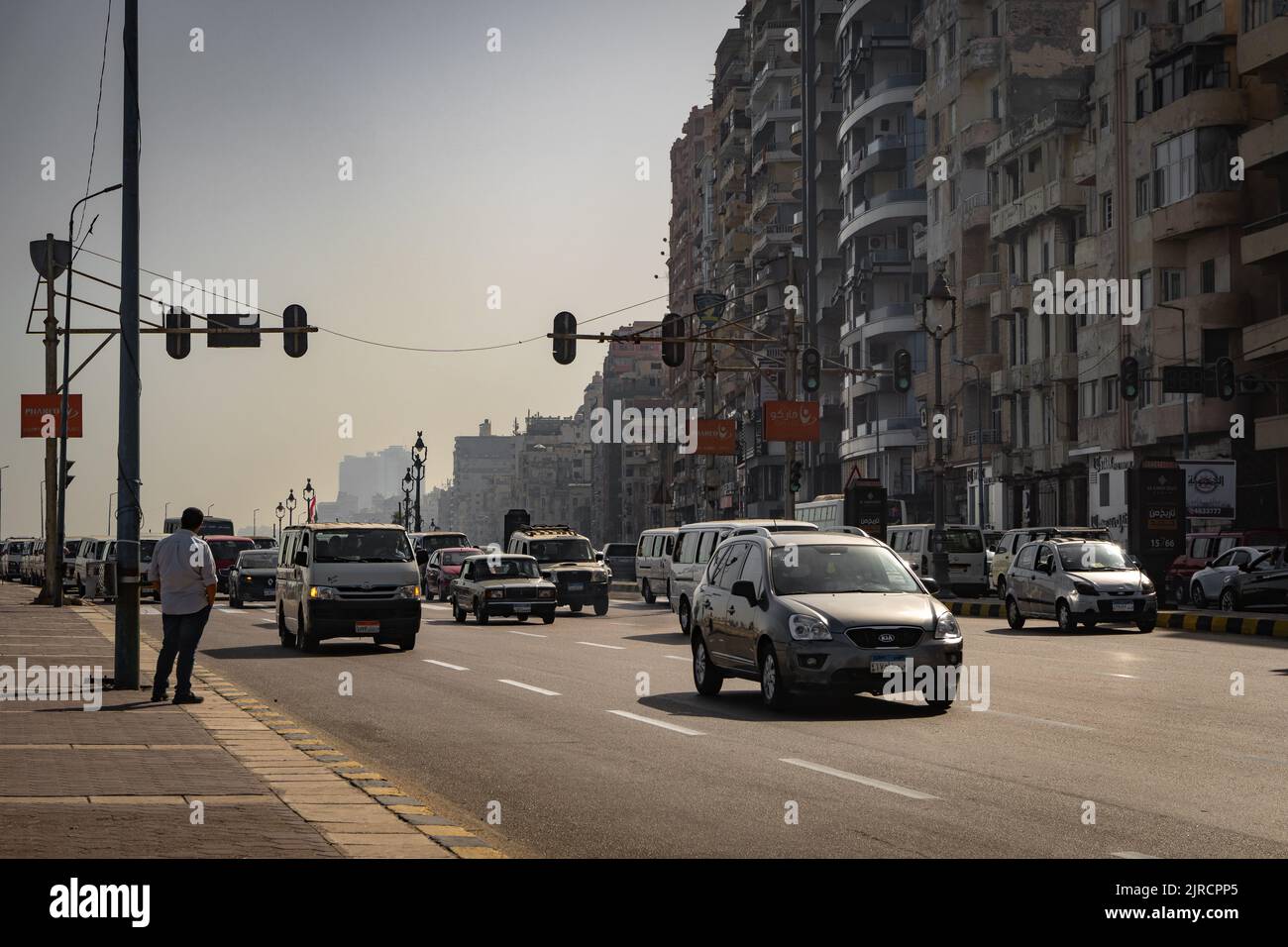 Una vista urbana di una strada piena di automobili e circondata da vecchi edifici e cartelli stradali ad Alessandria, Egitto Foto Stock