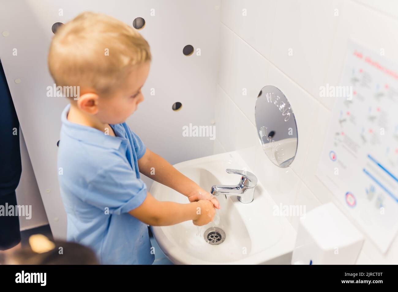 il bambino biondo si lava le mani nel bagno della stanza dei bambini. Foto di alta qualità Foto Stock