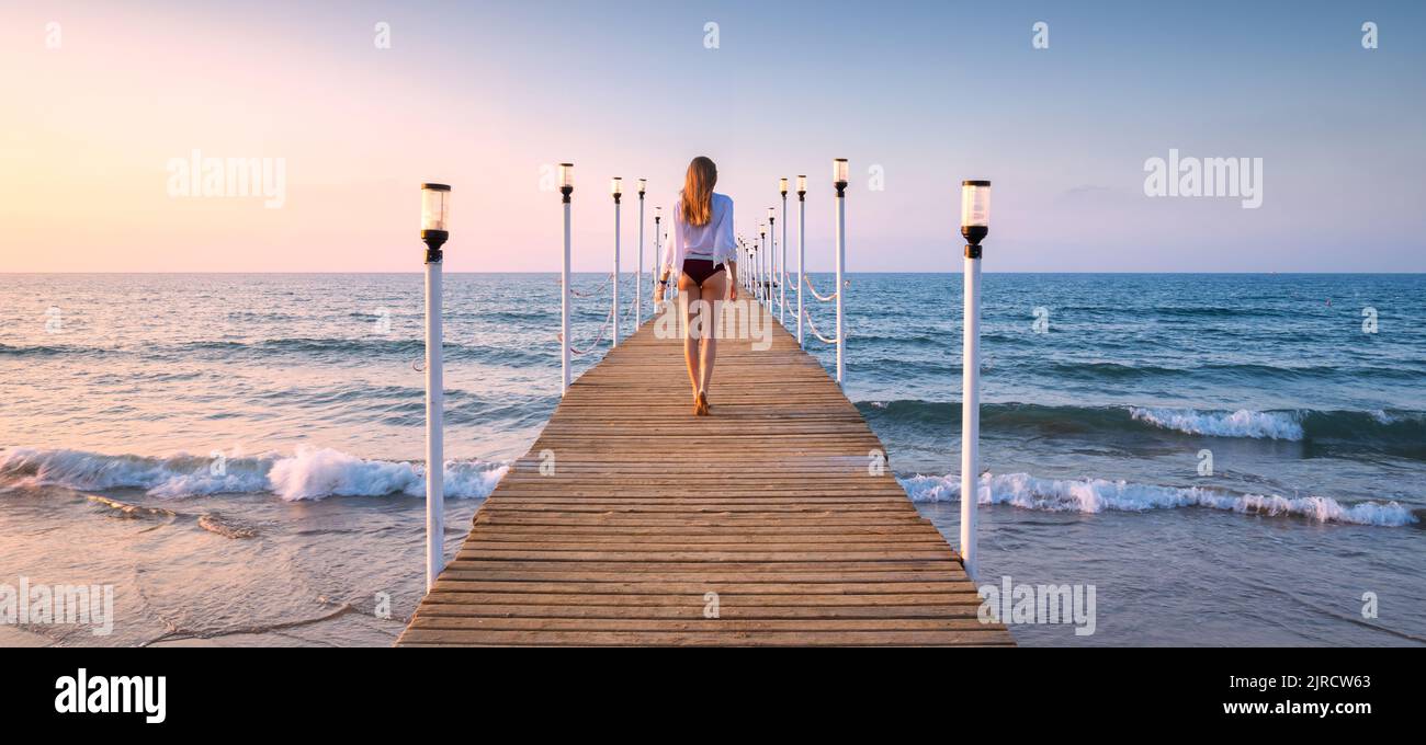 Felice giovane donna in bikini a piedi sul molo di legno sul mare Foto Stock