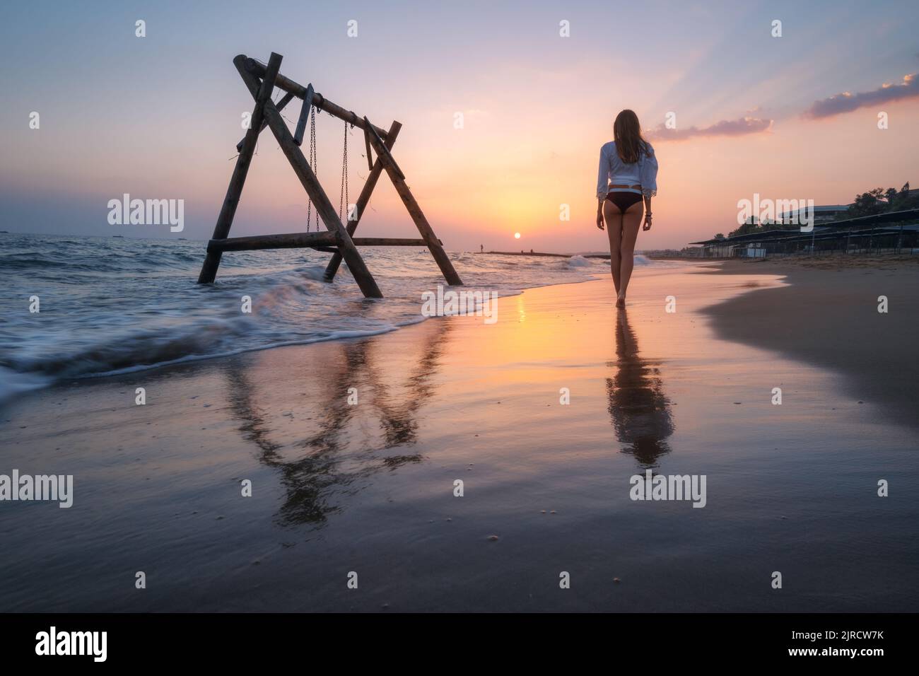 Giovane donna vicino altalena di legno in acqua, bel mare blu Foto Stock