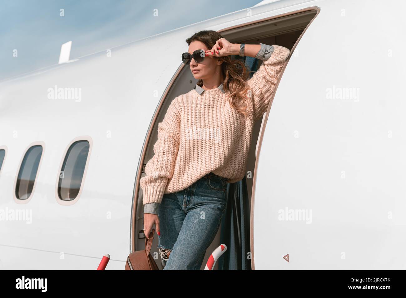 Donna passeggero negli occhiali da sole in piedi sulle scale dell'aereo all'aeroporto e guardando lontano Foto Stock