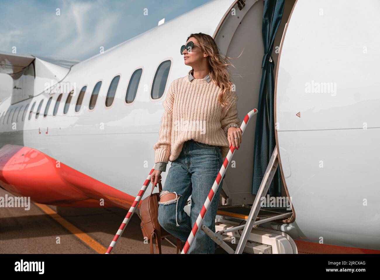 Donna passeggero negli occhiali da sole in piedi sulle scale dell'aereo all'aeroporto e guardando lontano Foto Stock