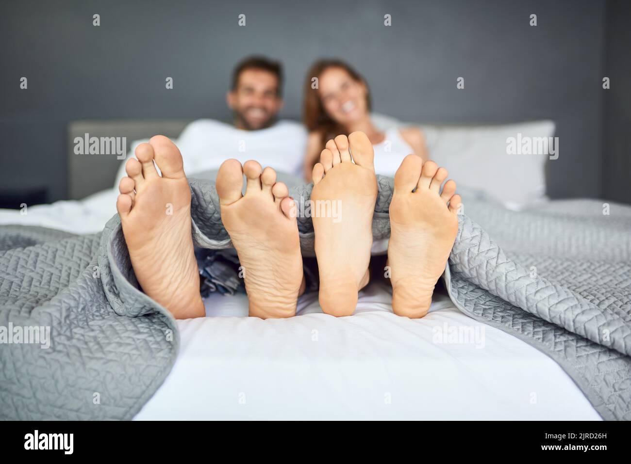 La domenica è il giorno del letto. Una giovane coppia felice che si rilassa a a letto con i piedi che scopano da sotto le lenzuola. Foto Stock