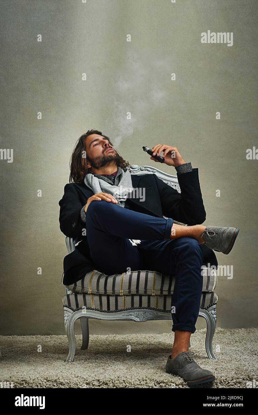 Il fumo non sembrava mai così bello: Un uomo elegante che fumava una sigaretta elettronica mentre era seduto in studio. Foto Stock