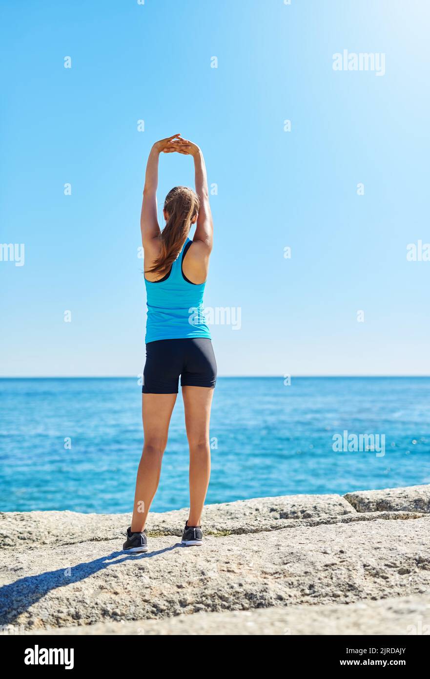 Raggiungere i suoi obiettivi di fitness. Una giovane donna che si allunga mentre fuori sulla spiaggia in una giornata di sole. Foto Stock