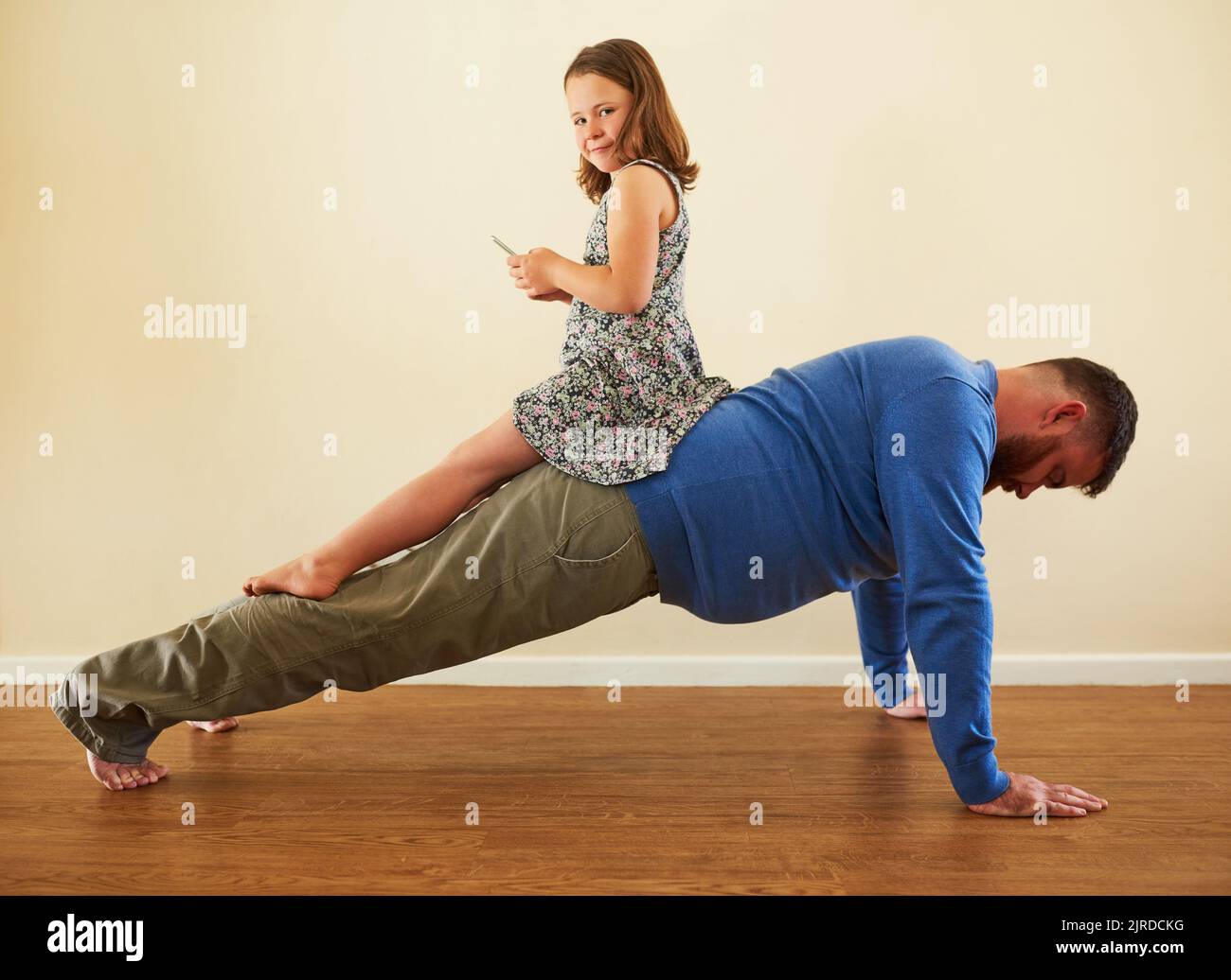Dice Daddy, meno telefono più fitness. Una ragazza adorabile che gioca con un telefono sulla schiena dei suoi padri, mentre lui funziona. Foto Stock