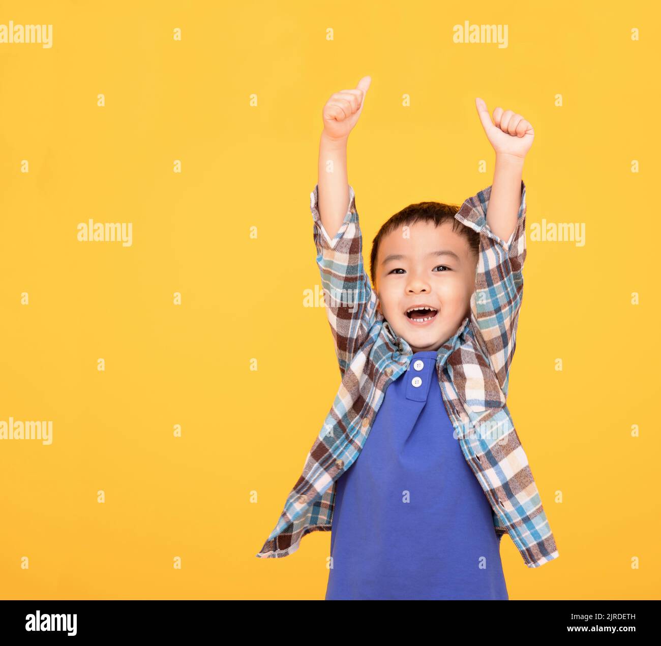 Felice ragazzo asiatico di fronte a sfondo giallo e mostrando pollici in su Foto Stock