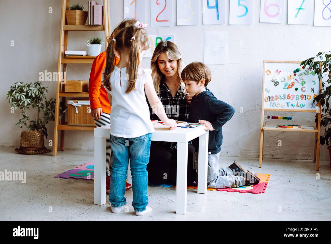Gruppo di bambini fantastici che studiano con l'aiuto di una maestra in classe. Studenti che imparano giochi da tavolo. Istruzione. Foto Stock