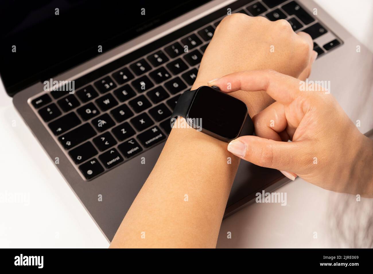 Utilizzando un moderno orologio intelligente, foto ravvicinata delle mani di una donna caucasica utilizzando un moderno orologio intelligente. Ha messo le mani sul suo laptop, controllando il battito del cuore. Foto Stock