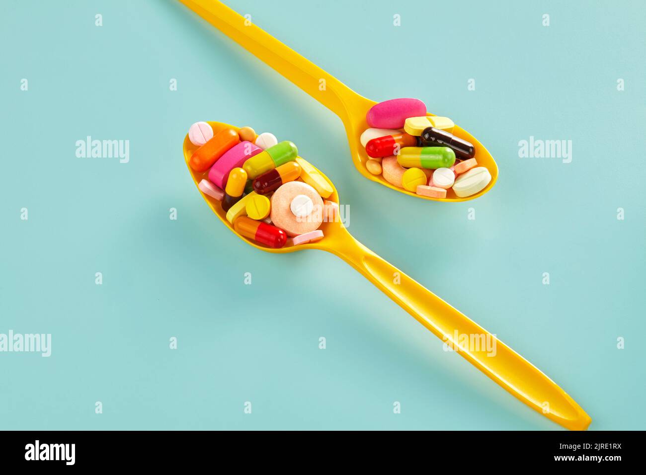 due pile di medicinali di forme e colori diversi su un cucchiaio di plastica gialla Foto Stock