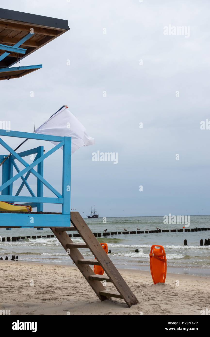 Una cabina di bagnino blu sulla spiaggia in una giornata nuvolosa. Scialuppa di salvataggio arancione bloccata nella sabbia accanto ad essa Foto Stock