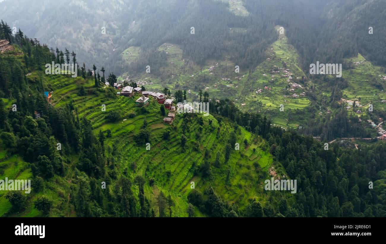 Cima aerea giù delle montagne di Jibhi sul pomeriggio nuvoloso e case che si affacciano sulla valle Foto Stock