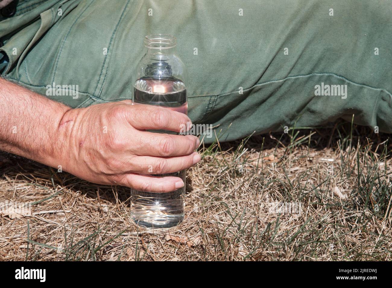 Il contadino siede sul suo prato e tiene in mano una bottiglia d'acqua. Foto Stock