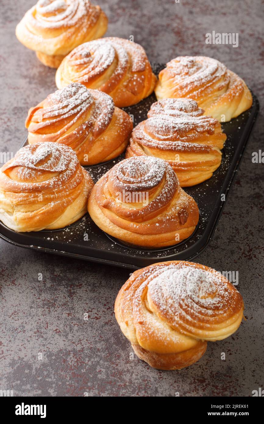 Crocini sfridati e burrosi e ricoperti di zucchero a velo nella teglia per muffin sul tavolo. Verticale Foto Stock