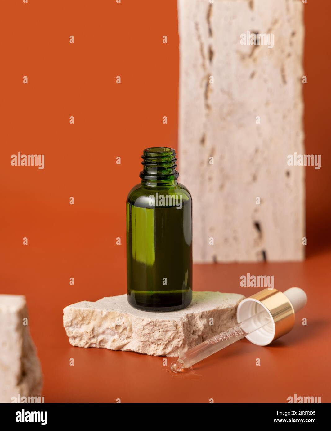 Flacone contagocce verde aperto su pietra beige su primo piano rosso, Mockup cosmetico. Prodotti di bellezza per la cura della pelle, siero o olio essenziale. Cosmetici naturali Foto Stock