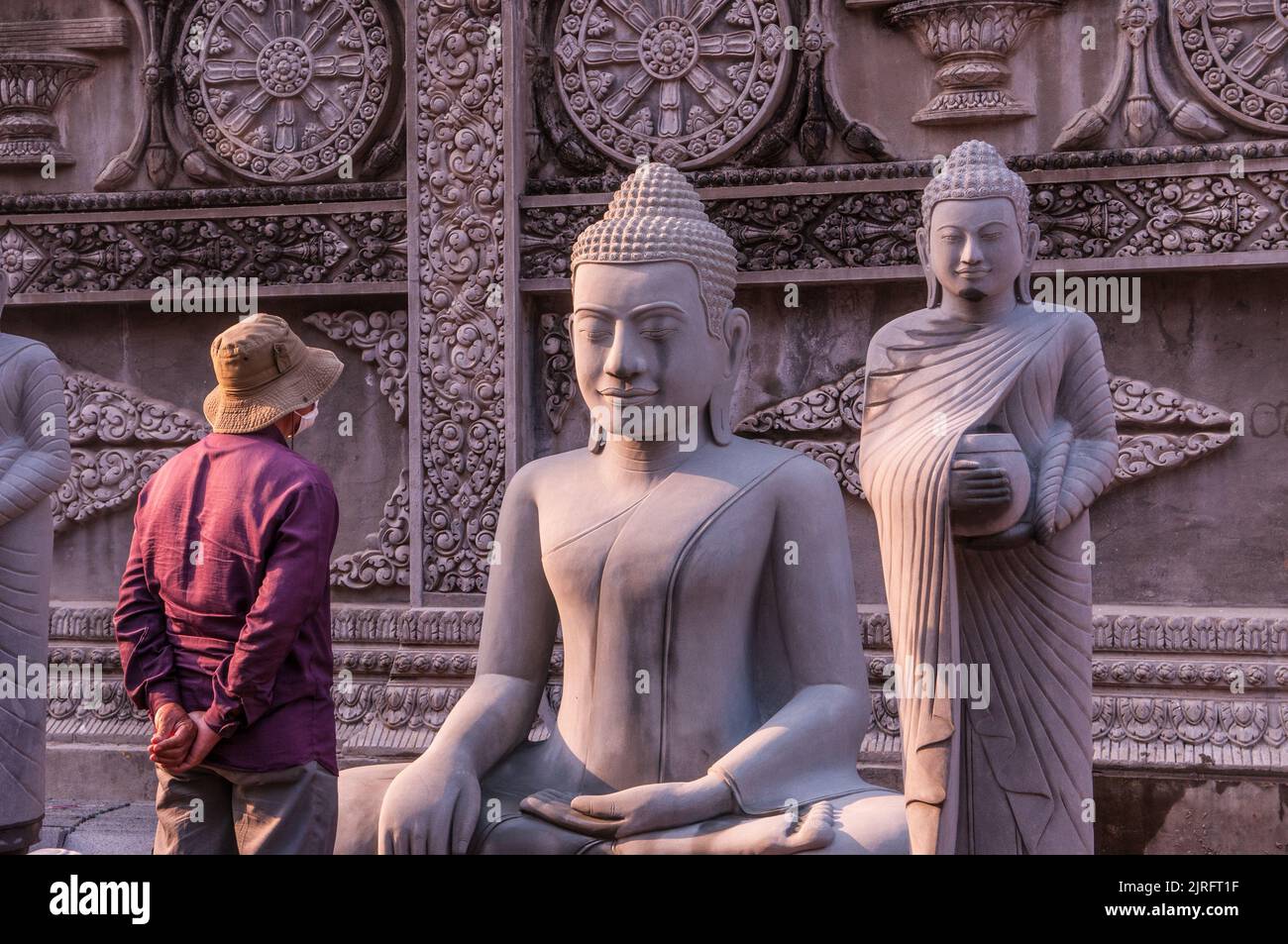 Durante un focolaio di COVID - 19, un uomo cambogiano, in una maschera di protezione del viso / copertura, contempla su una statua di Buddha durante la pandemia del coronavirus. Phnom Penh, Cambogia. 22 febbraio 2021. © Kraig Lieb Foto Stock