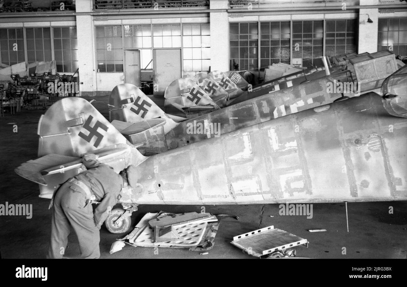 La Luftwaffe 1939 - 1945 Un soldato britannico esamina una fila di fusoliere Messerschmitt Me 109G parzialmente complete in un hangar all'aeroporto di Wunstorf, catturato dalla Brigata Parachute 5th, 6th Airborne Division, 8 aprile 1945. L'aeromobile è stato smontato e la verniciatura è stata tolta come parte di una ristrutturazione che non è mai stata completata. Foto Stock