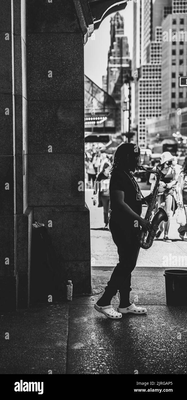 Uno scatto verticale in scala di grigi di un musicista che suona il sassofono per strada Foto Stock