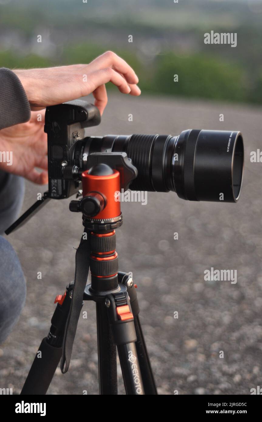 Una foto verticale di mani che azionano una fotocamera Olympus MFT in piedi su un treppiede con teleobiettivo Foto Stock