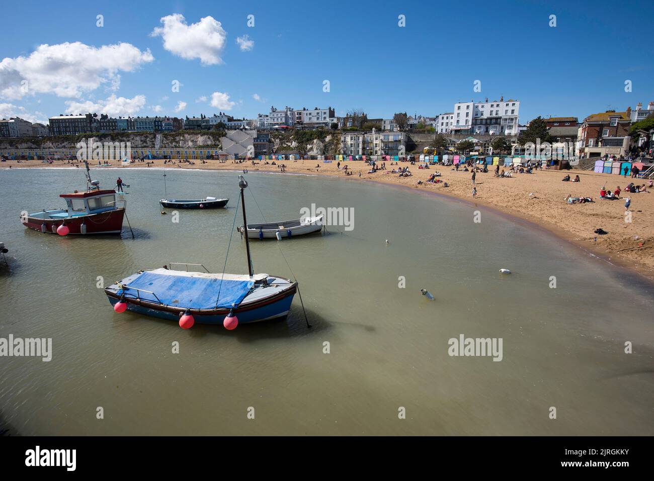 Barche all'ancora mentre la gente siede sulla spiaggia al sole a Broadstairs nel Kent Inghilterra Regno Unito Foto Stock